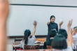 © pop_thailand - A smiling Asian female high school teacher teaches the white uniform students in the classroom by asking questions and then the students raise their hands for answers.