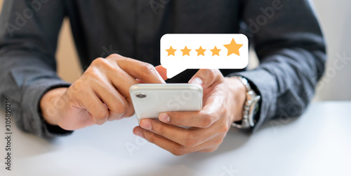 close up on businessman hand press on smartphone screen with gold five star rating feedback icon and press level excellent rank for giving best score point to review the service , technology business