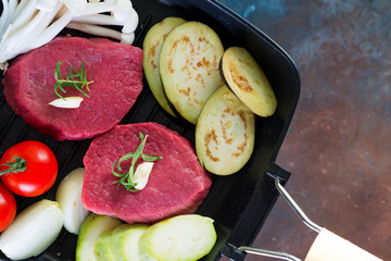 Poster - Raw juicy steaks in a pan ready for roasting on rustic concrete background. Fresh beef meat steaks with herbs, garlic,pepper, salt and tomatoes.