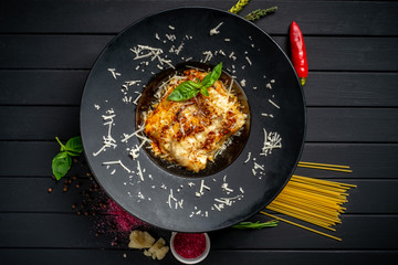 Meat lasagna with beef and tomato sauce on a black plate on a dark wooden background. The concept of Italian cuisine