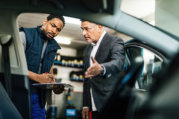 Wall Mural - African American mechanic and his customer examining car in auto repair shop.