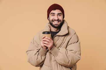 Poster - Image of young man in winter jacket and hat smiling while drinking coffee