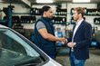 © Drazen - Young businessman shaking hands with African American auto mechanic at repair shop.