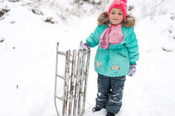 Wall Mural - Lovely smiling girl with frozen sled in her hand posing for camera in winter snowy day outdoor.