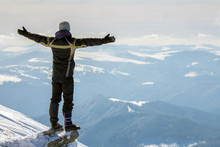 Silhouette Of Alone Tourist Standing On Snowy Mountain Top In Winner Pose With Raised Hands Enjoying View And Achievement On Bright Sunny Winter Day. Adventure, Outdoors Activities, Healthy Lifestyle.