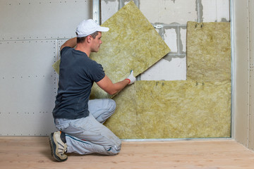 Worker insulating a room wall with mineral rock wool thermal insulation.