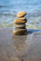 Five stones cairn tower, rock zen sculpture, brown beige pebbles and sea light blue background