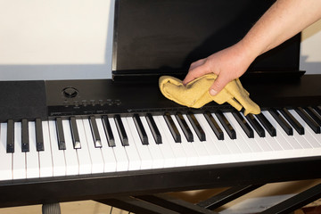 A male hand wipes dust off an electric piano.