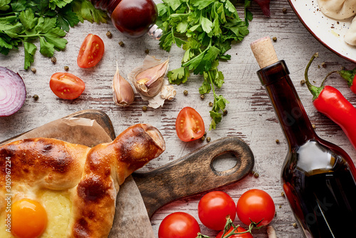 top-view-of-adjarian-khachapuri-wine-bottle-wegetables-and-cilantro-on-wooden-table