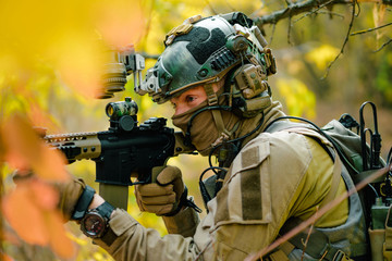 Wall Mural - Closeup man in uniform with machine gun in yellow forest. Airsoft soldier in forest side view