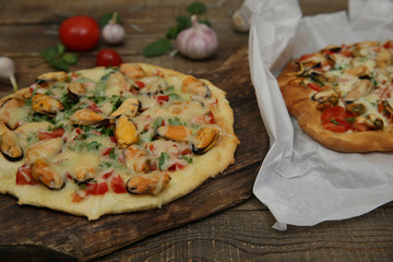 seafood pizzas with mussels, mozzarella cheese on a wooden board and pizza on a paper on a wooden rustic table. Mediterranean food. Vegetarian. 