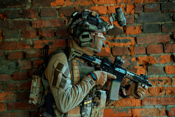 Wall Mural - Man in uniform with machine gun and night-vision device stand beside broken wall. Closeup irsoft soldier in night building