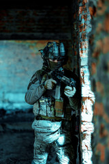 Man in uniform with machine gun and night-vision device stand beside broken wall. Airsoft soldier in night building. Vertcal photo