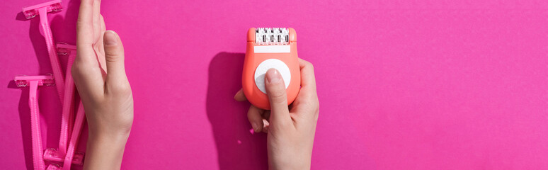 Wall Mural - cropped view of woman moving away disposable razors and taking epilator on pink background, panoramic shot