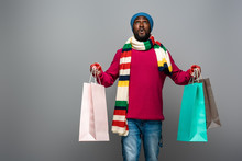 Shocked African American Man In Winter Outfit With Shopping Bags On Grey Background
