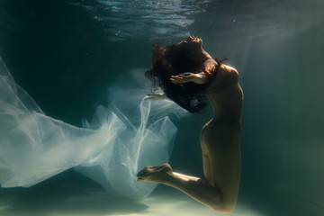 Beautiful girl swims underwater with long hair. Blue or gold background like gold. The atmosphere of a fairy tale or magic. Diving under the water with a shiny cloth