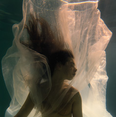 Beautiful girl swims underwater with long hair. Blue or gold background like gold. The atmosphere of a fairy tale or magic. Diving under the water with a shiny cloth