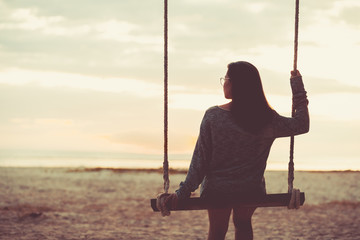 Single woman alone sitting  swinging on the beach sunset.are Lonely. style abstract Vintage tone