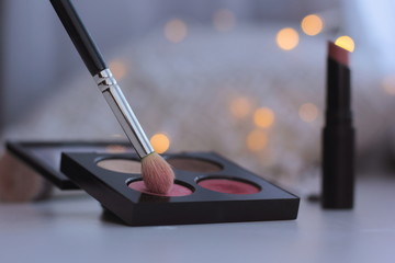 Wall Mural - Closeup of makeup brush and eyeshadow palette with fairy lights in the background. Concept of winter makeup.