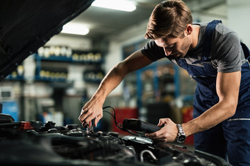 Wall Mural - Auto mechanic using diagnostic tool while repairing car engine in a workshop.