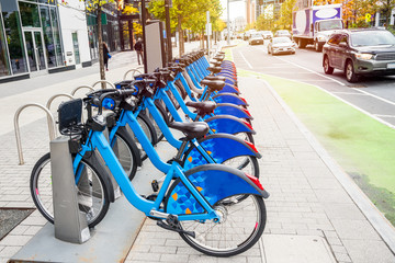 sharing bicycles in a docking station along a busy street with a bike lane in a downtown