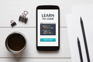 Wall Mural - learn to code concept on smart phone screen with office objects on white wooden table. top view