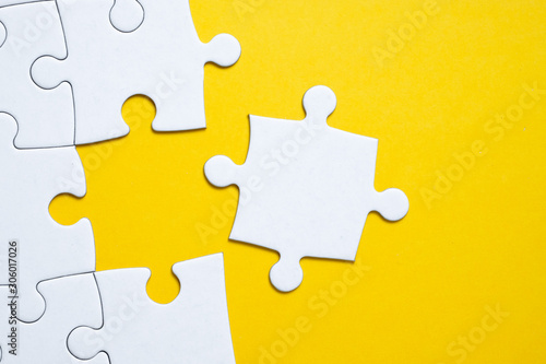 Final white piece is lying next to the jigsaw puzzle on yellow background Poster Mural XXL