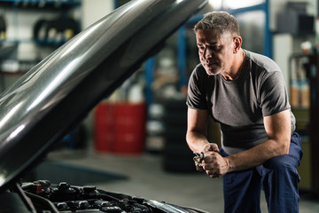 Wall Mural - Auto mechanic wiping hands after repairing car engine in a garage.