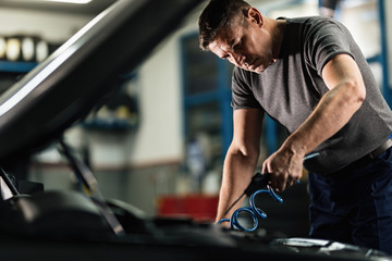 Wall Mural - Mid adult mechanic working on car engine in auto repair shop.