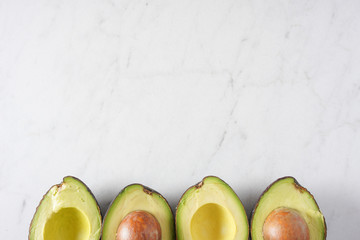 A row of cut avocados on a white marble background with copy space