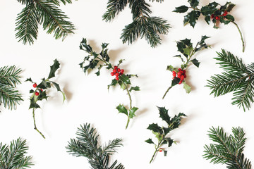 Wall Mural - Christmas natural floral pattern. Composition of red holly berries and green fir tree branches isolated on white table background. Winter natural decoration. Botanical festive flat lay, top view.