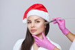 © Dimid - Cosmetologist does the procedure Microdermabrasion on the face of a beautiful woman in a Santa Claus hat. New Year's and Cosmetology concept.