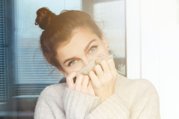 Winter portrait of a beautiful curly woman with blue eyes in a warm sweater with a pierced nose.