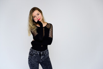 Concept of a woman talking to the camera. A photo of a pretty smiling girl with long beautiful curly hair in a black T-shirt on a white background is standing right in front of the camera.