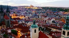 Aerial Footage Church Of Our Lady And Old Town District In Prague At Twilight. Drone Circling Near Towers And Spires Moving At Low Above Illuminated Streets And Buildings With Red Tiled Roof.