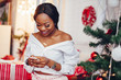 © prostooleh - Beautiful girl in a decorated room. Woman near Christmas tree. Black lady in a white blouse