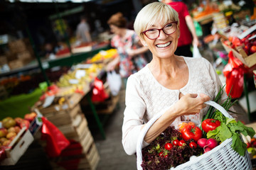 Picture of mature woman at marketplace buying vegetables