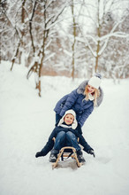 Beautiful Mother In A Blue Jacket. Family Sledding In A Winter Park. Little Boy In A Cute Hat