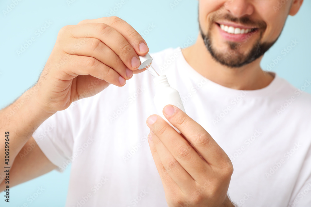 Handsome man with cosmetic product on color background, closeup