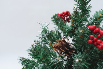 Merry christmas and a happy new year! Green Christmas tree lightly dusted with snow. Plastic Christmas tree on a light background with artificial berries and natural pine cones.