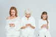 © LIGHTFIELD STUDIOS - granddaughter, mother and grandmother using smartphones isolated on grey