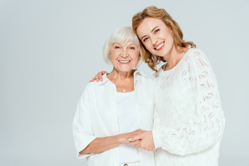 attractive daughter hugging smiling mother and looking at camera isolated on grey