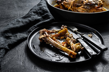 A plate of chicken bones and a chicken skeleton in a baking dish. Leftovers from dinner. Black background. Top view