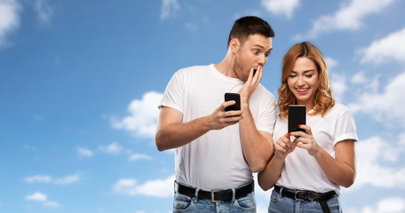 Poster - technology and people concept - happy couple in white t-shirts with smartphones over blue sky and clouds background