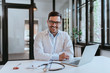 © bnenin - Portrait of a smiling doctor sitting at desk in the office.
