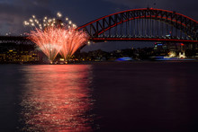 Red Stars Fireworks In Sydney Harbour With Boats And Parks Lights Behind. Australia.