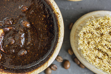 Coffee peeling. Coffee scrub in a wooden bowl with a wooden spoon on a dark background. Nearby is a bowl with coffee grounds, coffee grains, body brush and green flower leaves. Close-up 