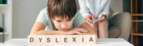 Fotografía panoramic shot of sad kid with dyslexia sitting at table with wooden cubes with