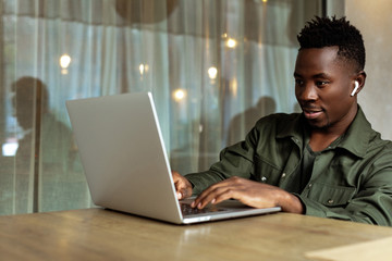 Sticker - Cheerful young african american man in headphones using computer in cafe