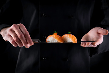 Sushi served on japanese knife in chef hands on dark background. Decorated salmon sashimi nigiri. Traditional japanese food. Copy space for text